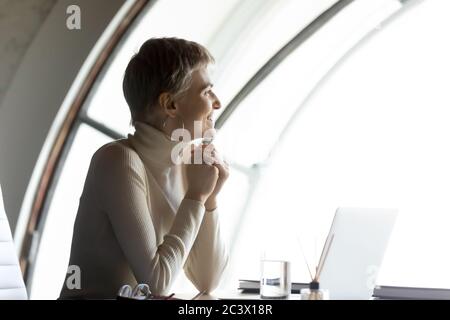 Businesswoman sitting at workplace finish workday look out the window Stock Photo