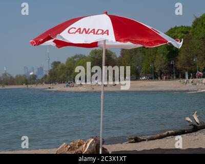 canadian flag patio umbrella a Canadian flag umbrella on the beach with the Toronto downtown skyline in  the distance for Canada Day celebration Stock Photo