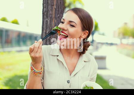 Happy Latina woman eating fresh salad outdoors in park Stock Photo