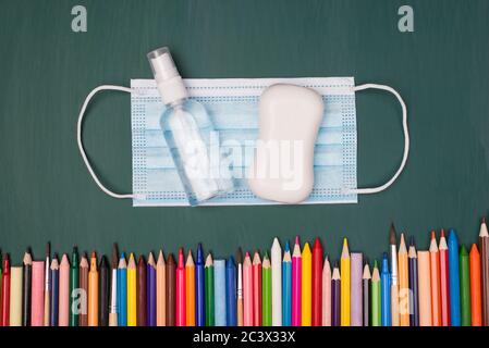 Home schooling concept. Top above overhead view photo of mask sanitizer soap and multicolored pencils and markers isolated on greenboard Stock Photo