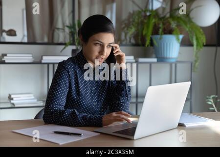 Indian businesswoman sit at workplace talking with client on phone Stock Photo