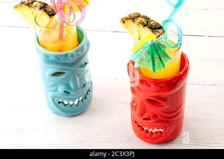 Hawaiian bar, summer vacation and beach drinks concept theme with Tiki mugs on white wood table with each mug having a plastic straw, a cocktail umbre Stock Photo