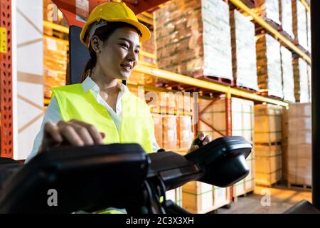 Portrait asian female warehouse worker using forklift truckin large warehouse distribution center. Business warehouse storage transportation and logis Stock Photo