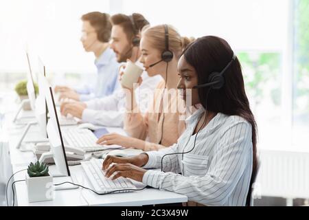 Line of call centre employees with headphones working on computers in open space office Stock Photo