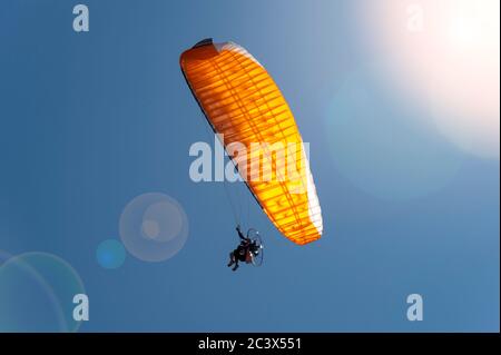 Motorised paraglider with blue sky and sun lens flare Stock Photo