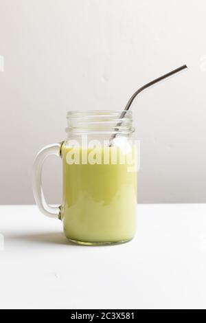 Matcha green tea latte in glass jar with metal tube on white background Stock Photo