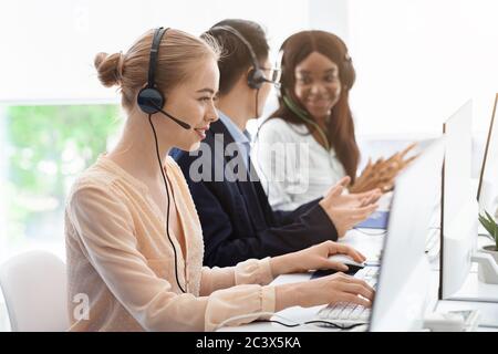 Team of call center operators in headsets speaking with customers at open space office Stock Photo