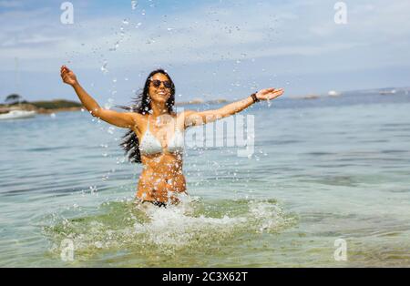 Tanned woman throwing water to the air in the beach, enjoying summer Stock Photo