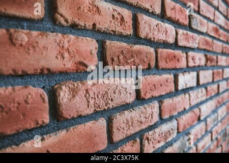 Side angle of a red brick wall. Close up view of cracked weathered cemented brickwork material. Modern interior design, unique perspective. Stock Photo
