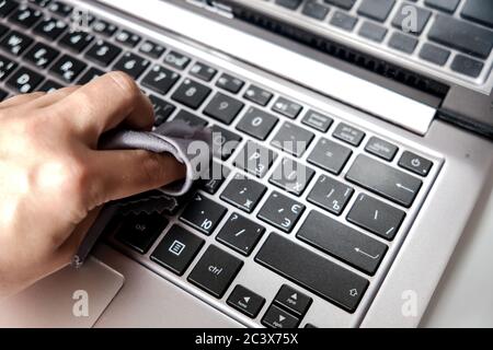 Cleaning the laptop keyboard with a napkin. Closeup white hand on computer. Removing dust and killing bacteria to stay safe at home. Stock Photo