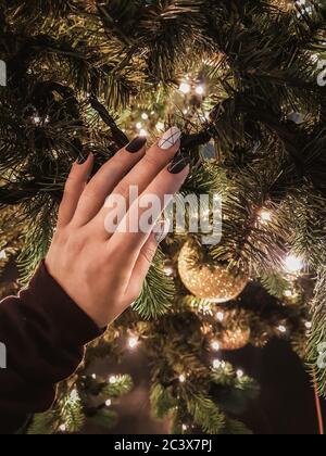 Woman's hand with beautiful black and white manicure touching Christmas tree with anticipation of New Year celebration. Festive happy mood. Close view Stock Photo