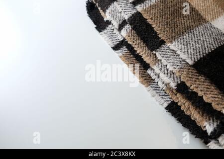 Folded plaid blanket with geometric pattern on a white table. Empty space for copy. Brown folds corner for lifestyle purposes. Soft woolen material Stock Photo