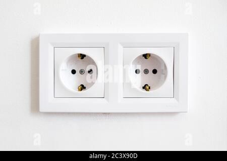 Pair of white European high voltage 220W sockets front on a white wall. Typical modern home interior. Essentials in redecorating and house remodeling.