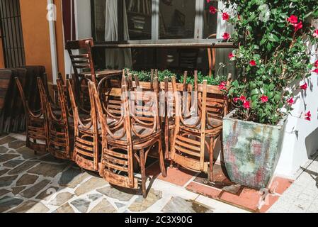 A bunch of stacked chairs near a closed cafe in Spain. Outside view on a sunny day. Early morning, no visitors, tourists around. Empty Spanish street Stock Photo