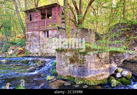 Old moss-covered stone in a river in front of a wooden ruin. Warnow Durchbruchstal in Mecklenburg-Vorpommern. Germany Stock Photo