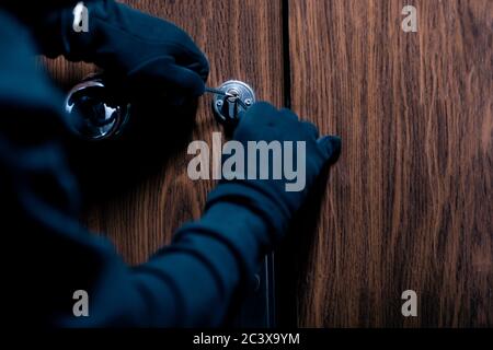 Robber in black mask cracking door with metal picklock Stock Photo