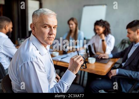 Serious Mature Entrepreneur Sitting At Corporate Meeting In Office Stock Photo