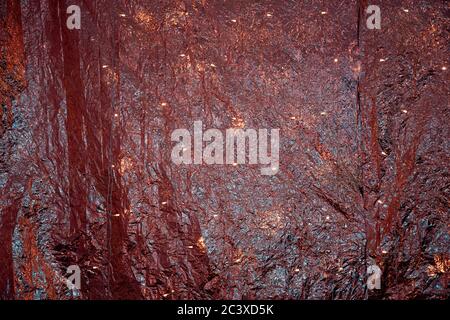 Red golden metallic rumpled foil backdrop with shiny lights.  Glitter texture of folded metallic fabric. Bright shimmer Christmas glowing background. Stock Photo