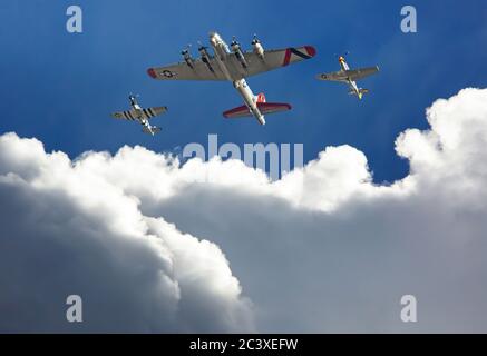 A B-17 'Flying Fortress' bomber is escorted by two P-51 Mustang fighters above dramatic clouds in a deep blue sky. Stock Photo