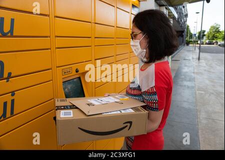 A Caucasian woman is picking up her shipment at an amazon locker. He holds the packaging with the logo in his hand and reads the communications on the Stock Photo