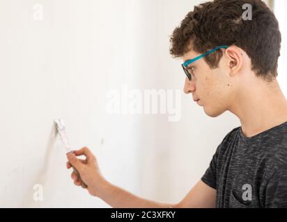Masonry work in the apartment: a Caucasian boy is intent on filling the imperfections of the wall. On the scraper there is a dose of putty paste that Stock Photo