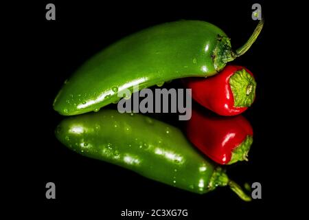 A vibrant Green Jalapeno pepper with water drops on it with a Bright Red Chili pepper on a reflective surface against a black field.  The peppers fill Stock Photo