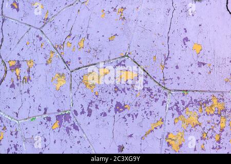 Flaking purple and yellow paint on old wall surface. Building facade with damaged paint. Abstract background, close-up, texture. Stock Photo