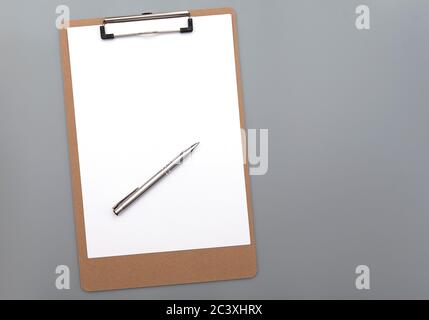 Paper clipboard with clean white blank paper and silver iron pen on gray background, top view