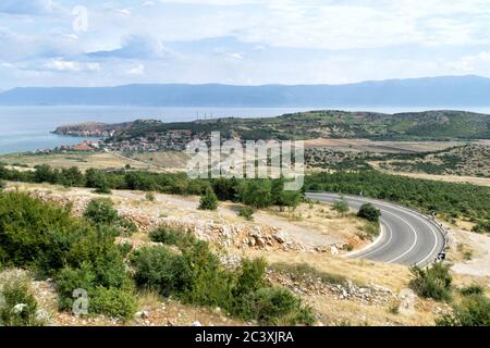 View from above on the Ohrid Lake, fishing village Lin and winding mountain road. Blue sky with white clouds. Albania, Europe. Stock Photo