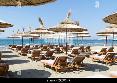 The rows of empty sunbeds with straw umbrellas on the beach. Blue sky and turquoise sea. Sunny summer day. Vlora / Vlore, Albania, Europe. Stock Photo