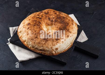 Round Armenian pita bread on a board and napkin on a dark background Stock Photo