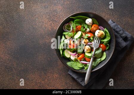 Salad with spinach, cherry tomatoes, onion and Mozzarella on brown. Top view. Stock Photo