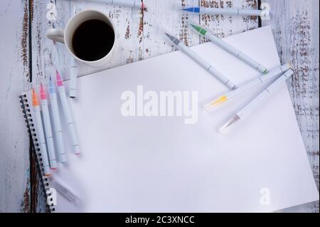 on an wooden table lies an album with many pens and markers and a cup of coffee. Stock Photo
