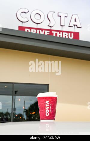 Talbot Green, Wales - June 2020: Cup of coffee on the roof of a car in front of a sign on top of a Costa Coffee shop with a drive through facility. Stock Photo