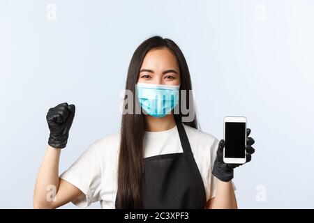 Covid-19 pandemic, coffee shop, small business and preventing virus concept. Cheerful happy cafe employee, barista in medical mask rejocing, showing Stock Photo