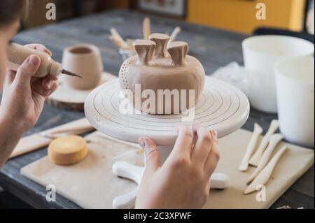 Closeup of bottom of mug, which is being decorated in ceramic studio. Female professional hands making clay dots or drops on the surface of vase by Stock Photo