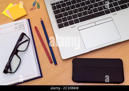 Top view of home office desk: laptop, smart phone, sticky notes, calendar, glasses, clips, colored pencils Stock Photo