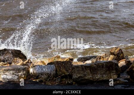 A splash of water flies into the air as waves hit rocks on a riverbank. Stock Photo