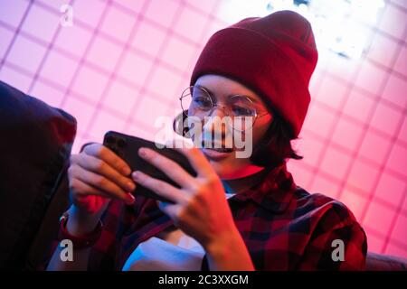 Teen girl exciting playing smart phone in a room lit with neon color at home. Stock Photo