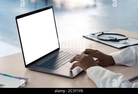 African doctor typing using laptop mock up white screen at desk, close up. Stock Photo