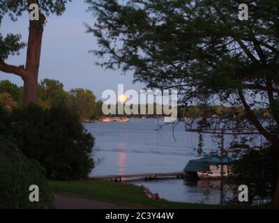 Moon Rising Through Pink Clouds Over a Lake Stock Photo