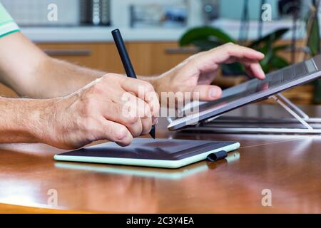 Male designer hands using a drawing graphics tablet and a laptop while working at home Stock Photo