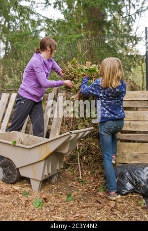 Woman and 10 year old daughter throwing thinned strawberry plants onto compost pile in Issaquah, Washington, USA Stock Photo