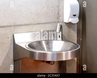 a stainless steel metal hand washing sink with hands free faucet as might be found in a factory or public washroom Stock Photo