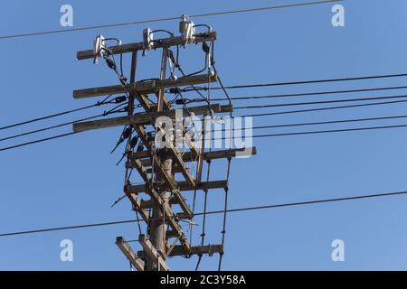 an old wooden electric power utility pole with a mess of wires and insulators on a blue sky Stock Photo