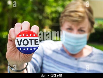 Portrait of woman wearing surgical mask holding Vote button Stock Photo