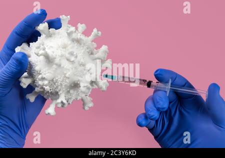 Hands in blue latex gloves holding Coronavirus model and syringe Stock Photo