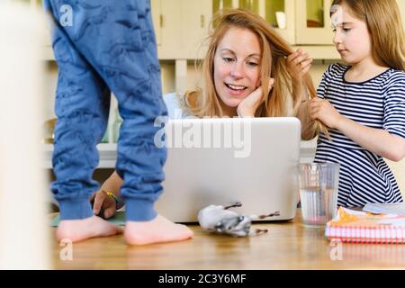 Woman working on laptop while son (4-5) and daughter (6-7) distracting her Stock Photo