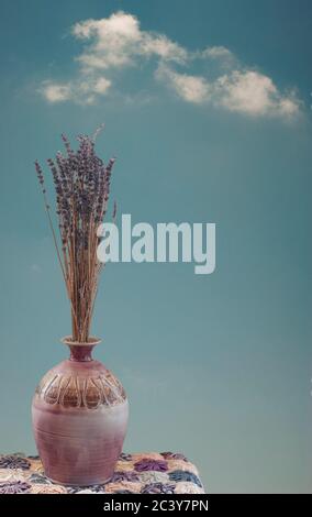 Tall bouquet of dried lavender stem flowers in ceramic pot with blue sky and clouds as background. Stock Photo