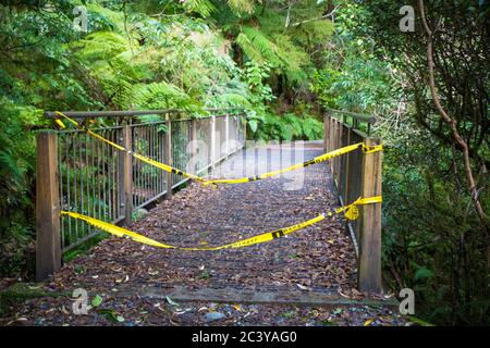 A Department of Conservation hiking track in Milford Sound has 'No Entry' tape across the bridge to signal hazards ahead with a washed out bridge Stock Photo